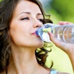 Девушка пьет воду из пластиковой бутылки