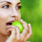 Красивая женщина кушает зеленое яблоко